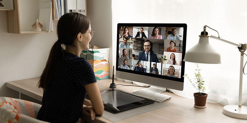 A rear view of a female remote employee holding an online video call with diverse colleagues illustrates remote employee monitoring.